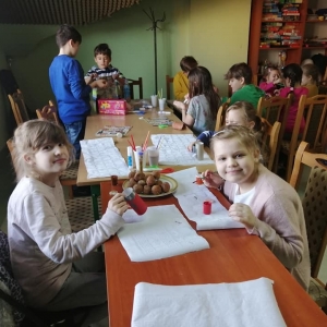 Dzieci siedzą przy stole zastawionym pączkami i przyborami plastycznymi.