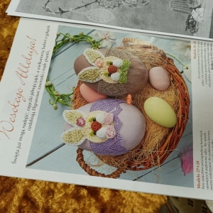 Kartka na złotym tle ze wzorem świątecznym pokazująca ubrane dwa jajka w wyszydełkowanych ubrankach w kształcie zajączka. 